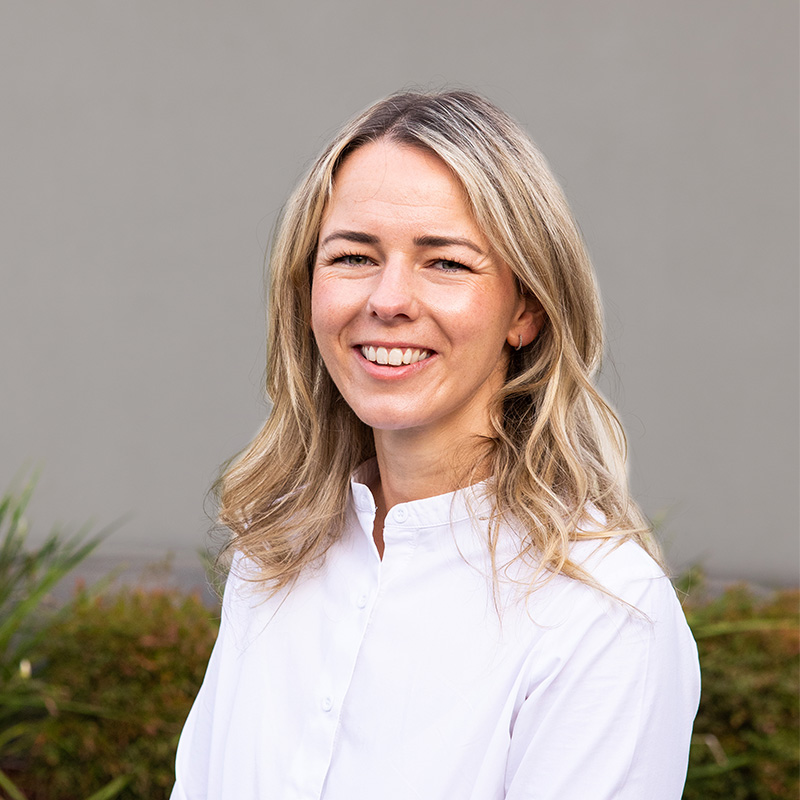 Photo of Dr Elly Burton, smiling, wearing a white shirt.