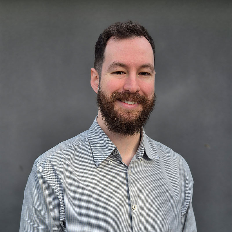 Photo of Dr Daniel Mulroyan, smiling, wearing a grey, textured shirt.