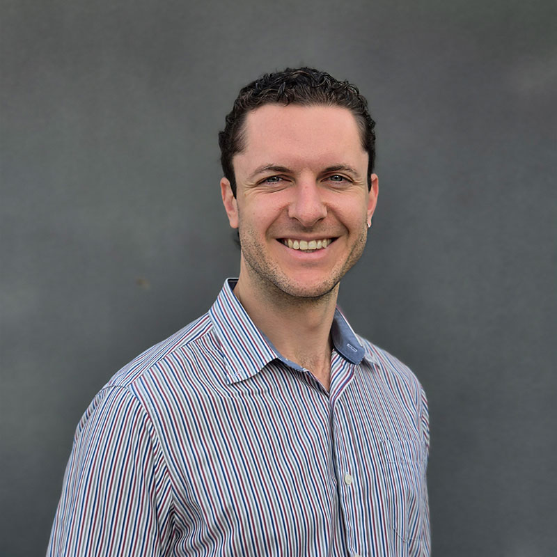 Photo of Dr Jake Mills, smiling, wearing a colourful, striped shirt.